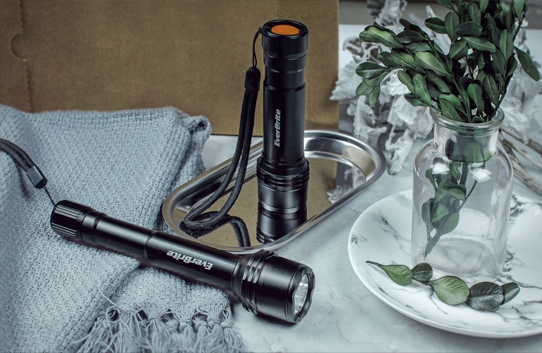 picture of flashlight on a desk beside a blanket and green leaves in a vase