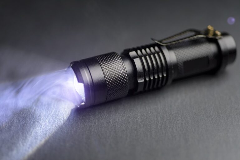 Tactical waterproof flashlight. LED flashlight shines on the table in smoke.